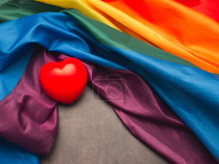 Foto de Un corazón rojo sobre la bandera del arco iris (LGBT). Vista superior. Acostado. Espacio para el texto. Concepto de amor. - Imagen libre de derechos