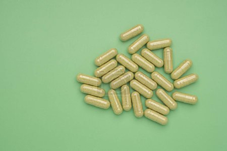 Flat lay of Andrographis paniculata capsules isolated on a green background. Space for text. Herbal, medicine, and healthcare concept