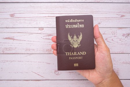 Photo for Hand holding Thailand passport with wooden wall background. Space for text. - Royalty Free Image
