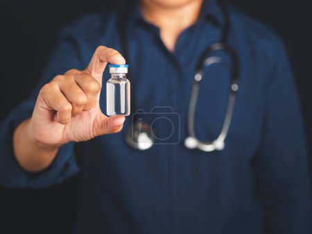 Photo for A doctor is holding a vaccine bottle while standing in the studio with a black background. Vaccine for prevention and treatment from virus infection. Concept of medical and the fight against the virus. - Royalty Free Image