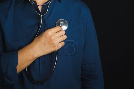 Hand of a doctor holding a stethoscope to checking heart self while standing in the studio with a black background. Space for text. Close-p photo.