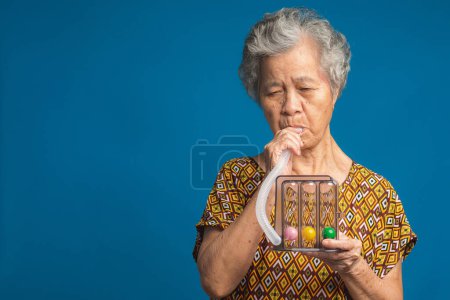 Téléchargez les photos : Équipement de spiromètre incitatif pour aider à effectuer des exercices de respiration profonde. Femme âgée l'utilisant pour améliorer son haleine. Utile pour les affections pulmonaires comme la maladie pulmonaire obstructive chronique. - en image libre de droit