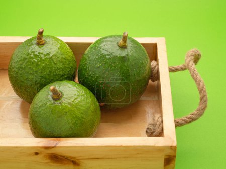 Avocados liegen isoliert in einer Holzkiste auf grünem Hintergrund. Nahaufnahme. Konzept der gesunden Früchte.