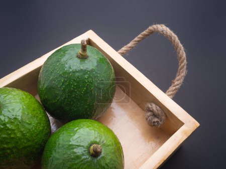 Avocados liegen isoliert in einer Holzkiste auf schwarzem Hintergrund. Nahaufnahme. Konzept der gesunden Früchte.