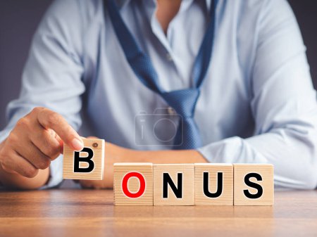 Businessman hand to pick up a wooden cube with the word Bonus while sitting in the office. Close-up. Receive bonuses, rewards. Bonus wage for holidays, benefits, cashback. Business concept.