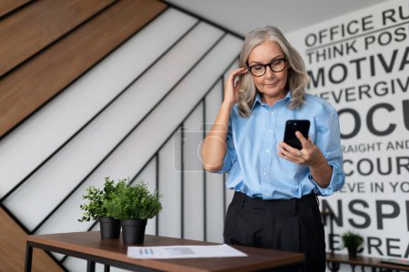 Photo for Business Caucasian woman with glasses watching mobile phone in the office. - Royalty Free Image