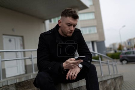 Téléchargez les photos : Jeune homme assis et regardant le téléphone mobile à l'extérieur. - en image libre de droit