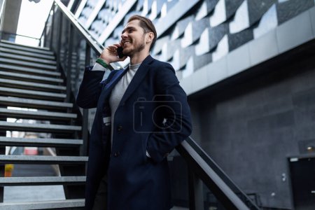 Téléchargez les photos : Succès caucasien homme d'affaires parle sur un téléphone portable sur le fond d'un bâtiment moderne. - en image libre de droit