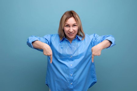 Téléchargez les photos : Jeune femme blonde européenne en chemise décontractée montre les mains vers le bas à baner sur fond bleu avec espace de copie. - en image libre de droit