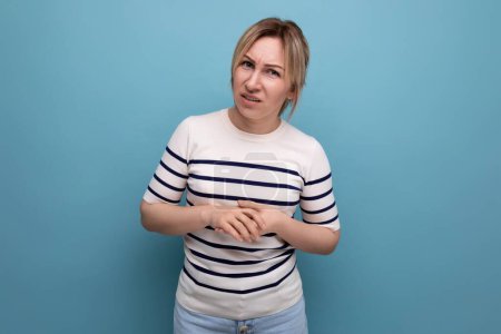 Téléchargez les photos : Douteux blond jeune femme dans un pull rayé regarde suspicieusement sur un fond bleu avec espace de copie. - en image libre de droit