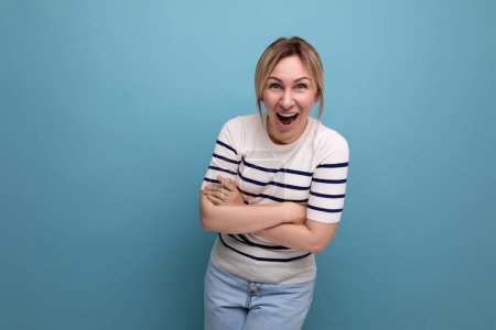 Foto de Foto horizontal de brillante mujer rubia feliz en traje casual riendo con entusiasmo sobre fondo azul con espacio de copia. - Imagen libre de derechos