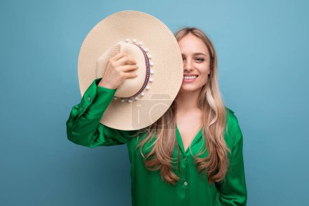 Foto de Foto horizontal de una mujer encantadora de vacaciones en un sombrero de paja de verano sobre un fondo de estudio azul. - Imagen libre de derechos