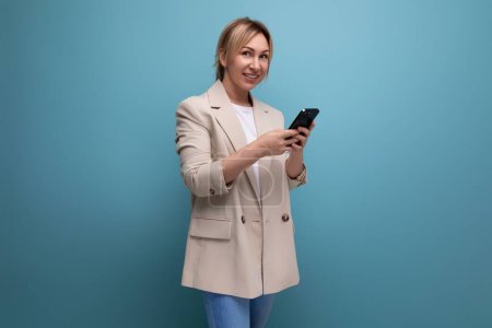 Téléchargez les photos : Blonde jeune femme dans une veste sur le shopping au téléphone sur un fond de studio. - en image libre de droit
