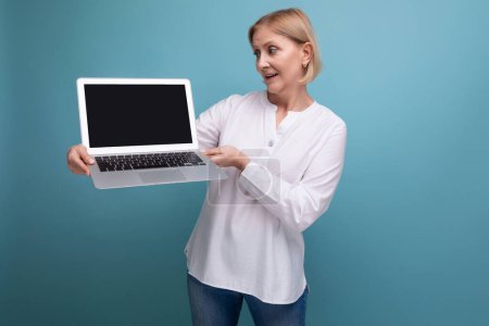 Foto de Éxito años 50 mujer de mediana edad con el pelo rubio demuestra un ordenador portátil con mocup. - Imagen libre de derechos