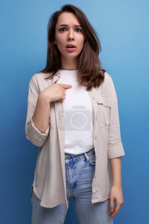 Téléchargez les photos : Bouleversé surpris jeune brunette adulte féminin en chemise décontractée sur fond bleu. - en image libre de droit