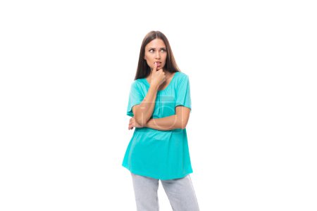 Foto de Mujer morena caucásica joven pensativa con el pelo largo en una camiseta azul sobre un fondo blanco con espacio para copiar. - Imagen libre de derechos