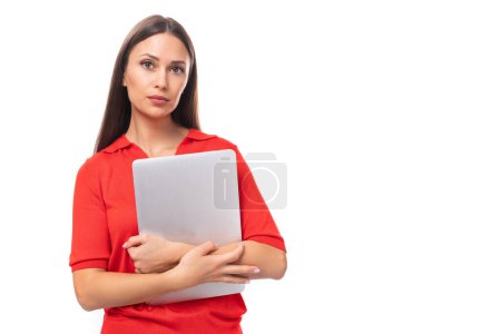 Téléchargez les photos : Jolie femme caucasienne aux cheveux noirs habillée d'un chemisier à col en V rouge tenant un ordinateur portable pour travailler au bureau. - en image libre de droit