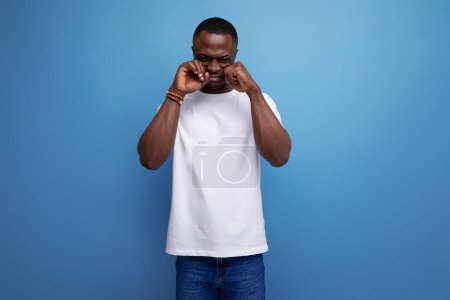 Téléchargez les photos : Bouleversé jeune homme africain en t-shirt blanc sur fond studio avec espace de copie. - en image libre de droit