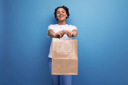 Photo for Young happy brunette woman with afro hair in a white tank top holding a craft pait from a delivery service. - Royalty Free Image