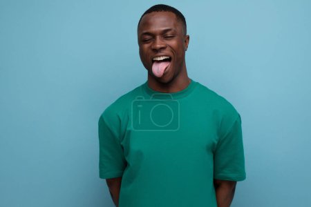 Téléchargez les photos : Drôle jeune américain en t-shirt fait une grimace sur un fond bleu avec espace de copie. - en image libre de droit