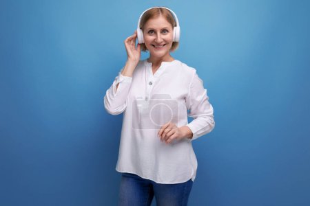 Téléchargez les photos : Femme mature avec coiffure blonde dansant sur la musique dans les écouteurs sans fil. - en image libre de droit