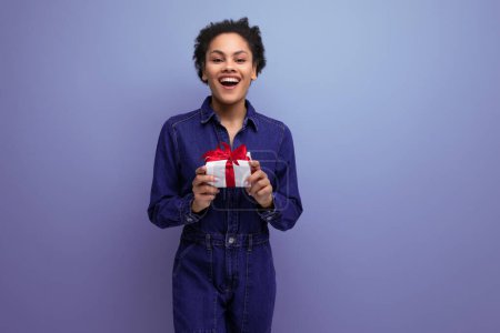 Téléchargez les photos : Jeune femme latine brune mince vêtue de salopettes en denim bleu a reçu un cadeau d'anniversaire. - en image libre de droit