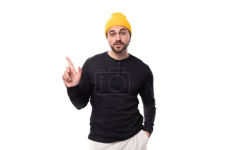 Téléchargez les photos : Smart authentique brunet mâle adulte dans un pull noir parle d'une idée sur un fond blanc avec espace de copie. - en image libre de droit