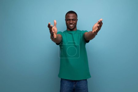 Téléchargez les photos : Jeune positif amical africain gars avec une coupe de cheveux courte habillé dans un t-shirt de base sur le fond avec espace de copie. - en image libre de droit