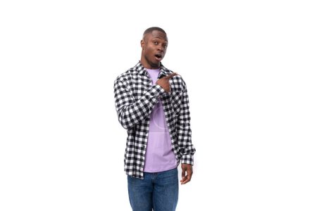 Foto de Un africano confuso de 30 años de edad, vestido con una camisa a cuadros blanco y negro encoge los hombros contra el fondo con espacio para copiar. - Imagen libre de derechos