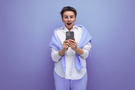 Téléchargez les photos : Énergique positive jeune femme brune avec coupe de cheveux courte en chemise blanche bavarder dans le smartphone. - en image libre de droit