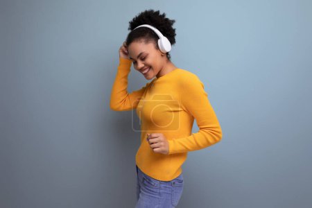 Foto de Joven mujer latina con cabello afro escuchando música con auriculares en el fondo del estudio. - Imagen libre de derechos
