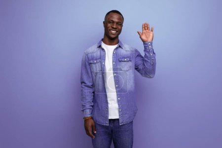 Téléchargez les photos : Beau jeune homme américain en jean veste salue souriant sur fond bleu avec espace de copie. - en image libre de droit