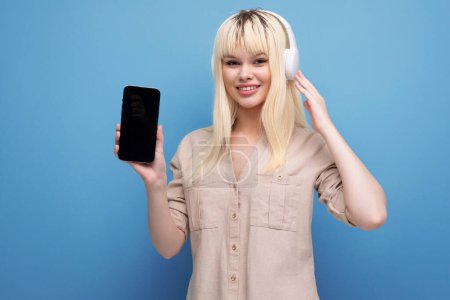 Téléchargez les photos : Charmante jeune fille blonde aime écouter podcast avec écouteurs. - en image libre de droit