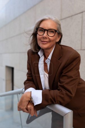 Photo for Close-up portrait of a charming slim mature woman with gray hair in a stylish suit on the street. - Royalty Free Image