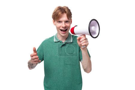 Téléchargez les photos : Jeune homme européen aux cheveux roux rapporte avec enthousiasme les nouvelles à travers un mégaphone. - en image libre de droit