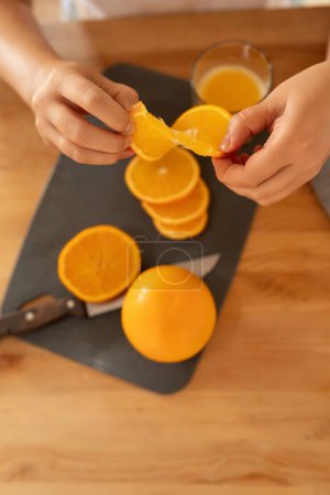 Foto de Manos de una mujer sosteniendo una jugosa naranja sentada en la cocina. - Imagen libre de derechos
