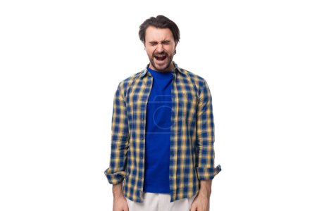 Foto de Un joven caucásico brutal hombre con una cara sin afeitar vestido con una camisa a cuadros azul emocionalmente grita con los ojos cerrados. - Imagen libre de derechos