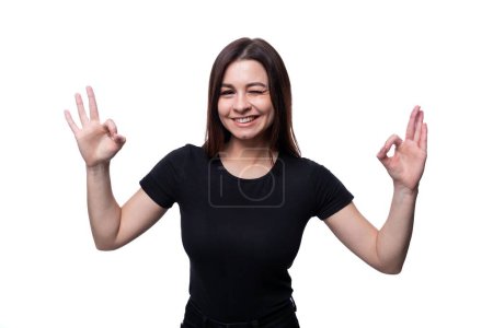 Photo for Positive pretty young brunette woman wearing a black t-shirt showing ok gesture. - Royalty Free Image
