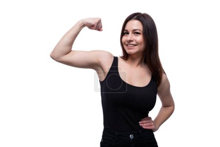 Glückliche junge stilvolle Frau mit schwarzen Haaren, die starke Muskeln zeigt.