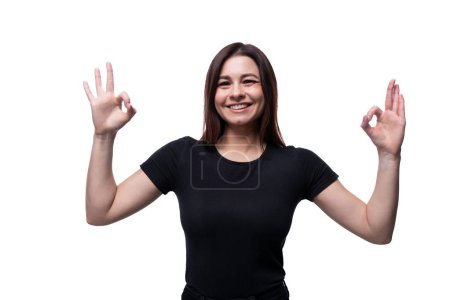 Photo for Caucasian cute young woman with black hair wearing a black T-shirt shows an excellent gesture. - Royalty Free Image
