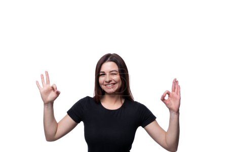 Photo for Young confident woman with black hair dressed in a black T-shirt shows her hands up. - Royalty Free Image