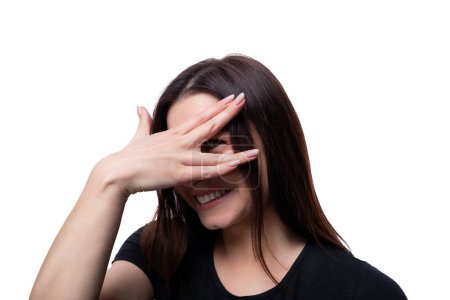 Photo for Caucasian cute young woman with black hair wearing a black T-shirt is embarrassed and covers her face. - Royalty Free Image