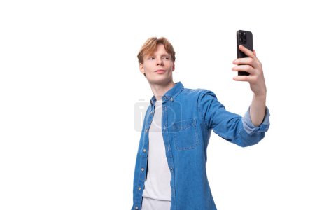Téléchargez les photos : Un jeune Européen fort confiant aux cheveux dorés vêtu d'une chemise en denim bleu prend un selfie. - en image libre de droit