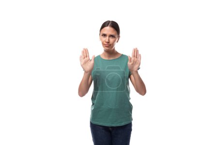 Photo for A 30 year old slender European brunette woman with a ponytail dressed in a green t-shirt and jeans is trying to remain calm. - Royalty Free Image