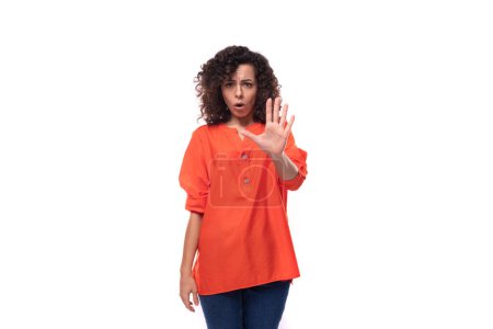 Foto de Joven mujer europea confundida con el pelo negro rizado en una camisa naranja se siente sorprendido. - Imagen libre de derechos