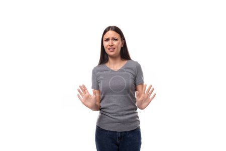 Foto de Retrato de una mujer joven delgada caucásica en una camiseta gris muestra un gesto de desacuerdo y rechazo. - Imagen libre de derechos