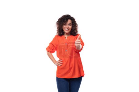 Foto de Joven y elegante morena caucásica rizada vestida con una blusa naranja señala con su dedo índice. concepto publicitario. - Imagen libre de derechos
