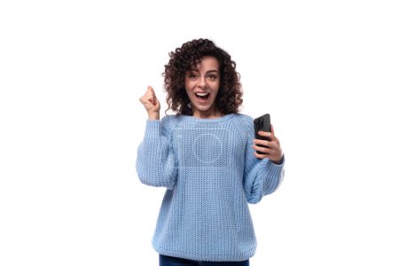 Photo for Young pretty woman with curly method hairstyle smiling holding smartphone in her hand. - Royalty Free Image