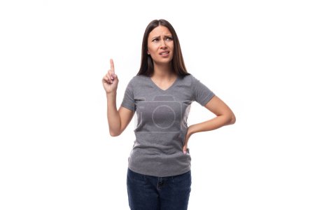 Téléchargez les photos : Jeune femme promotrice brune surprise vêtue d'un t-shirt gris sur fond blanc. - en image libre de droit