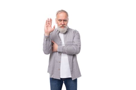 Téléchargez les photos : Homme âgé bien soigné avec une barbe grise et la moustache est habillé d'une chemise à carreaux et un jean sur un fond blanc avec espace de copie. - en image libre de droit